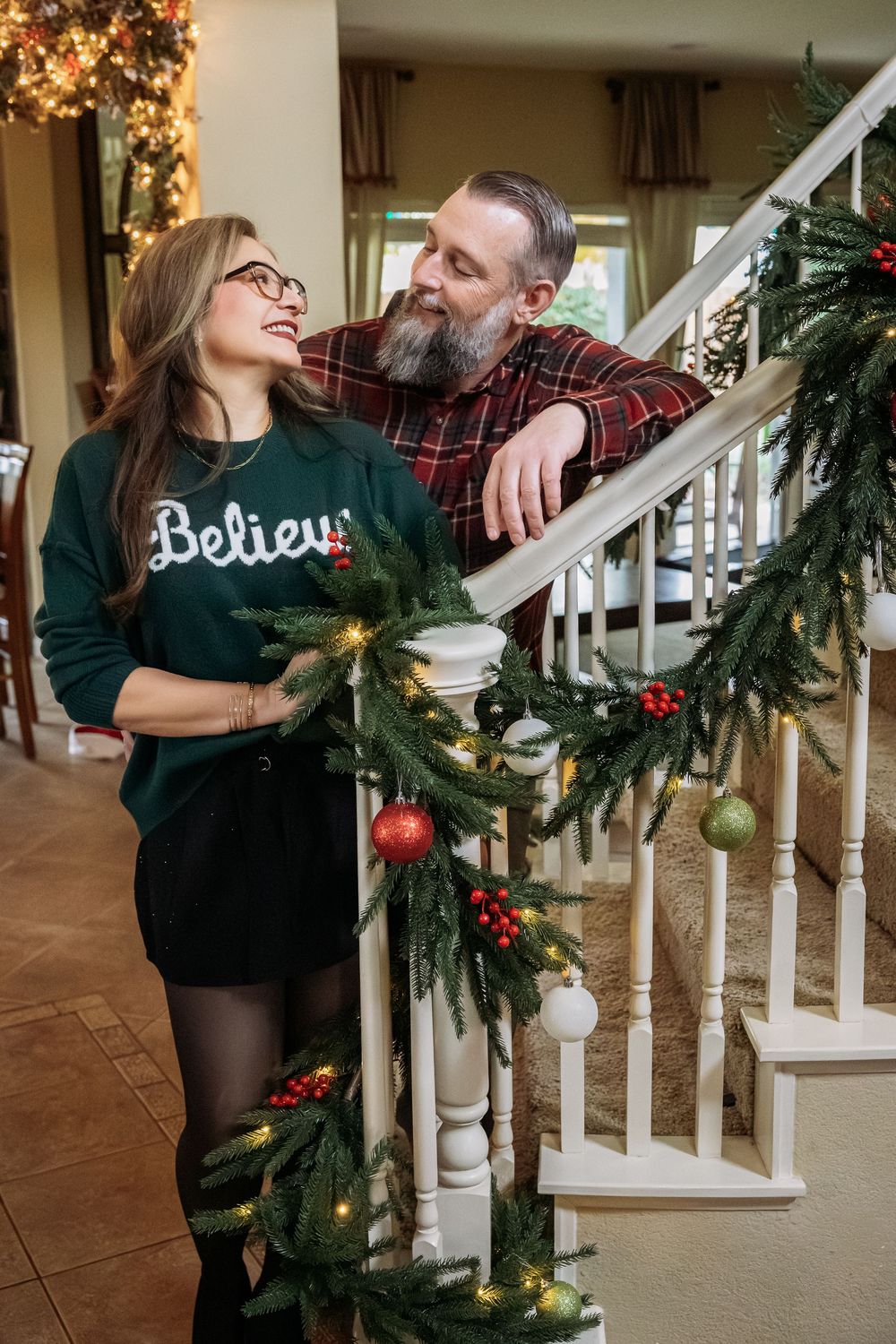 A couple decorates their staircase with festive Christmas garland and ornaments while sharing a joyful moment together.