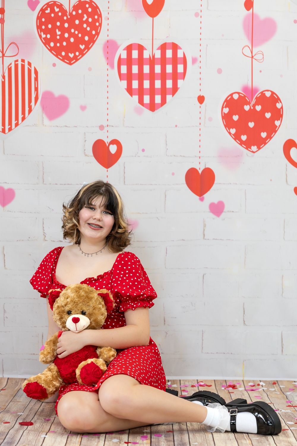 Valentine's day themed photo with red and pink heart decorations on white brick wall background with teddy bear.