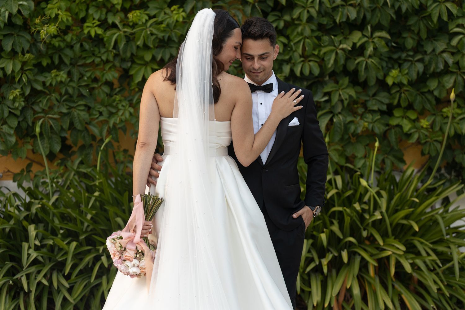 Wedding couple poses in garden setting with lush greenery backdrop.