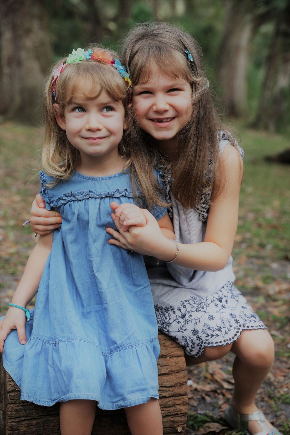 Two young children in blue dresses embrace while playing outdoors.