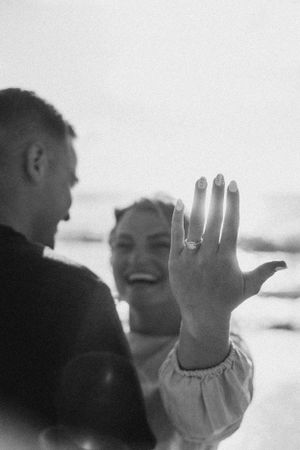 A hand displaying an engagement ring against a bright background during a beach proposal photoshoot.