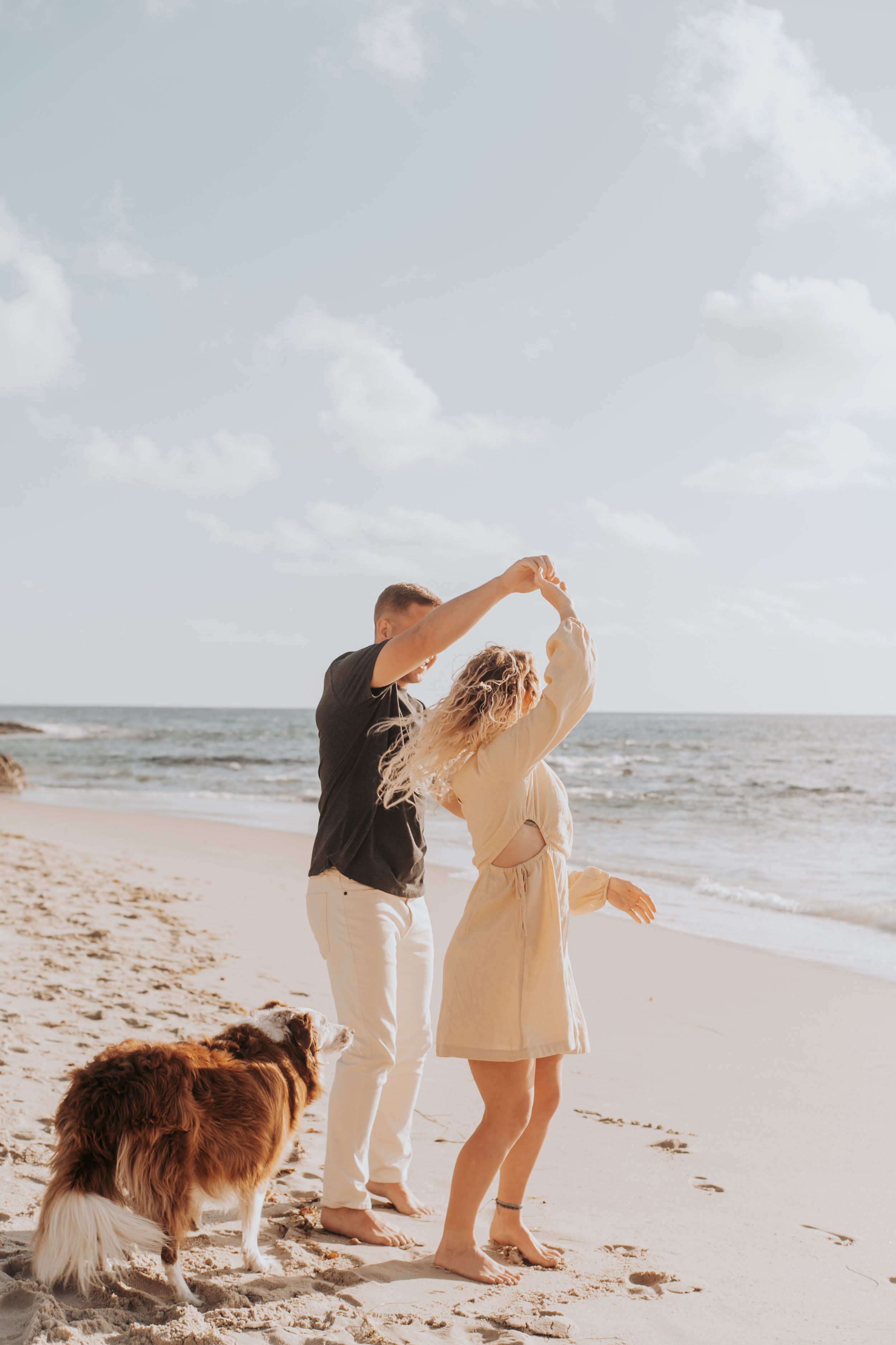 Couple dancing on beach at sunset with dog watching their romantic moment.