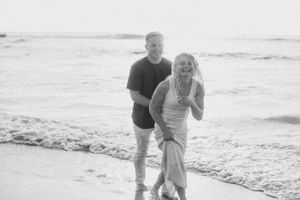 A joyful couple celebrating their engagement while walking along the beach.