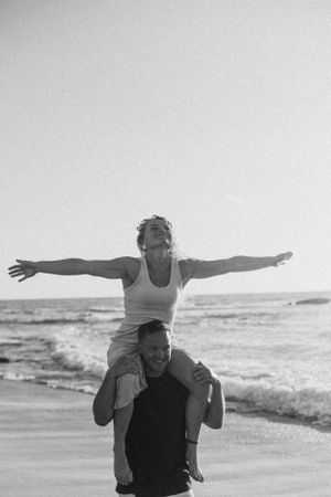 Couple enjoying a fun piggyback ride along the shoreline in black and white.