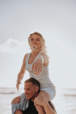 Playful couple celebrating their engagement with piggyback rides on the beach.