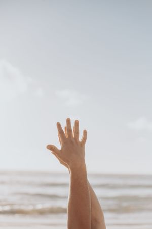 Hands raised joyfully against a bright, cloudy beach sky.