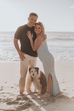 Happy couple poses with their furry companion on sunny beach.