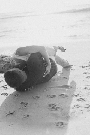 Black and white photo of couple embracing on beach sand.