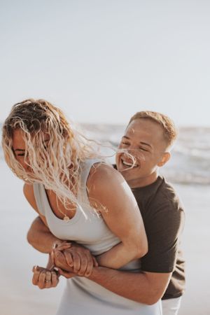 A joyful candid moment captured on the beach showing playful laughter and embrace.
