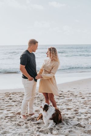 Intimate beachside moment between couple with their dog sitting at their feet.