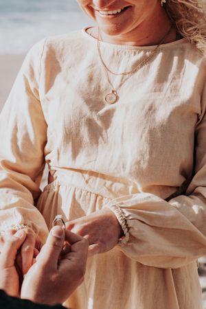 Close-up of hands holding an engagement ring against a cream colored dress.
