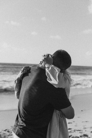 A black and white photo capturing an intimate moment between two people embracing on the beach.