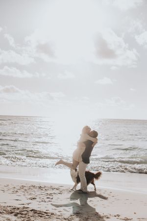 A joyful embrace on the beach at sunset with a dog nearby.