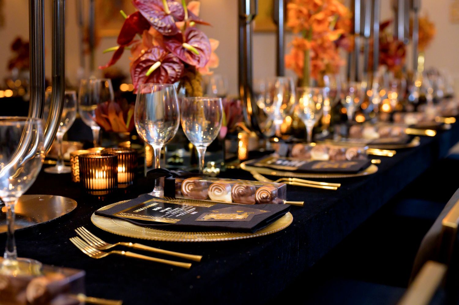 Elegant dinner table setting with dark black linens, glowing candles, crystal glasses and pink floral centerpieces.