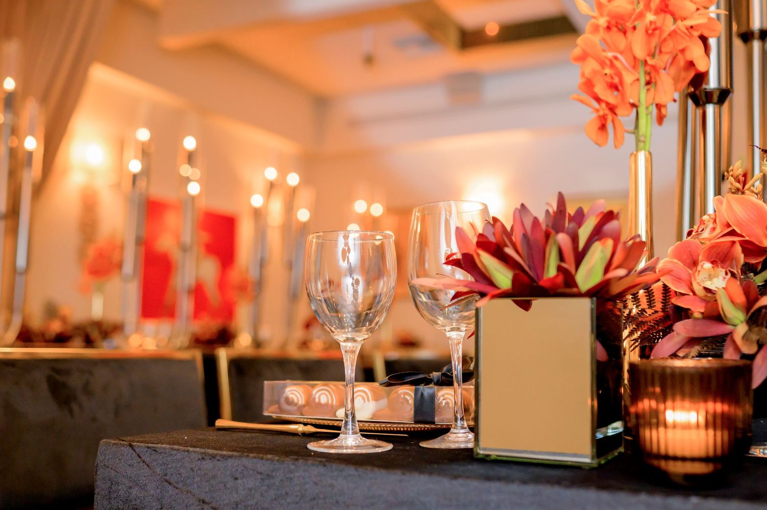 Elegant table setting with wine glasses and coral floral arrangements illuminated by warm candlelight in an upscale venue.