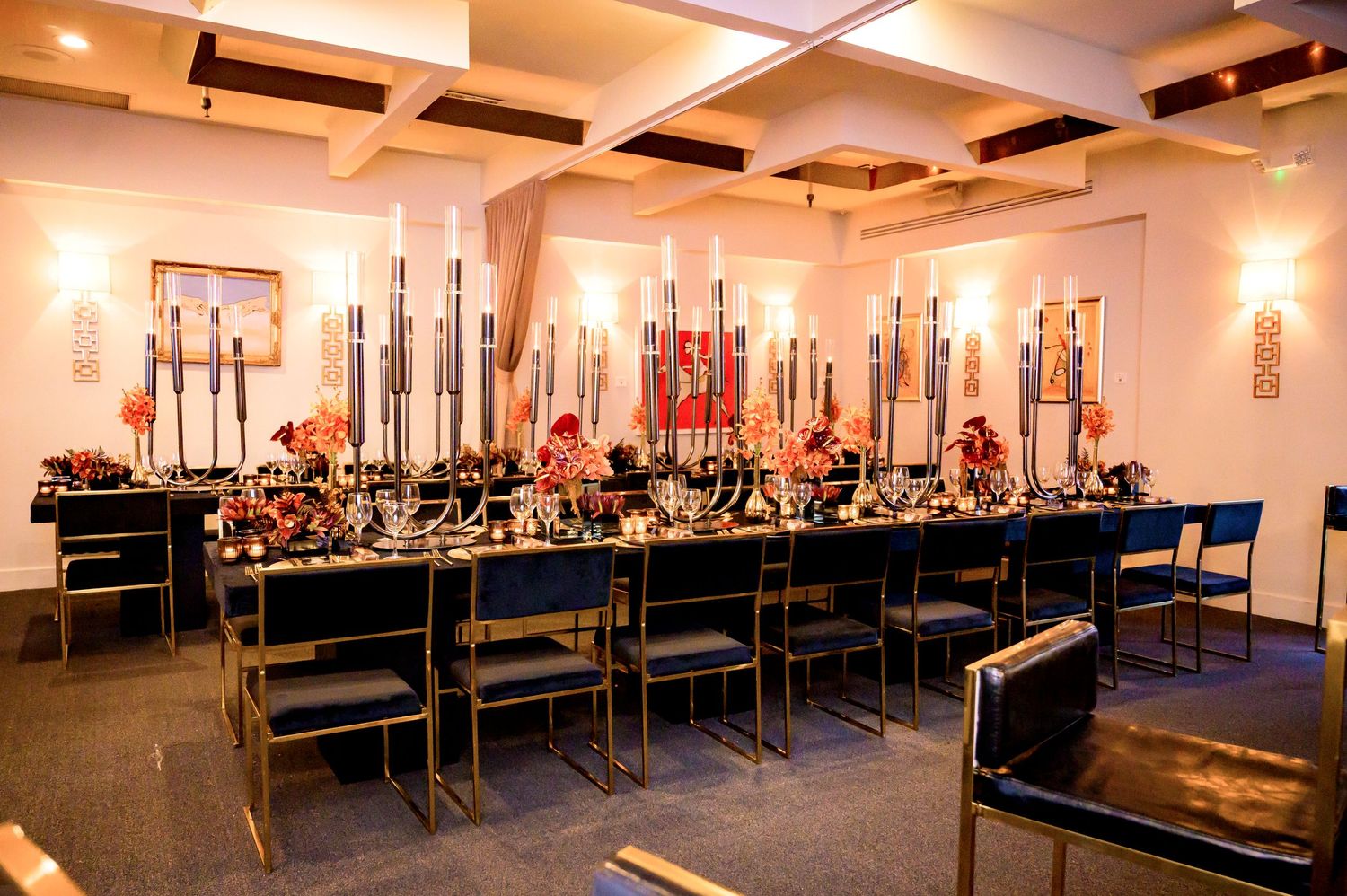 An elegant banquet table setup with tall candle centerpieces and blue chairs in a modern event space.