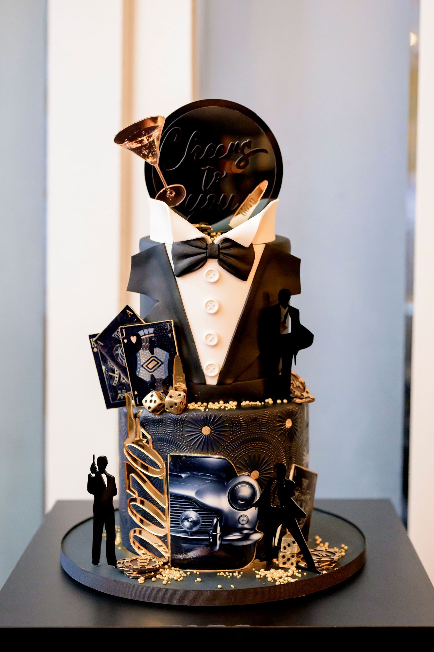 Elegant black and gold art deco themed wedding cake with tuxedo design, vintage car details and champagne accents.