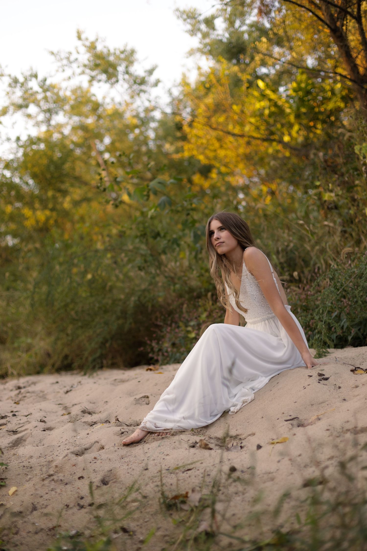 Teenage girl basking in the sand on the creekbank during her high school senior portriats.