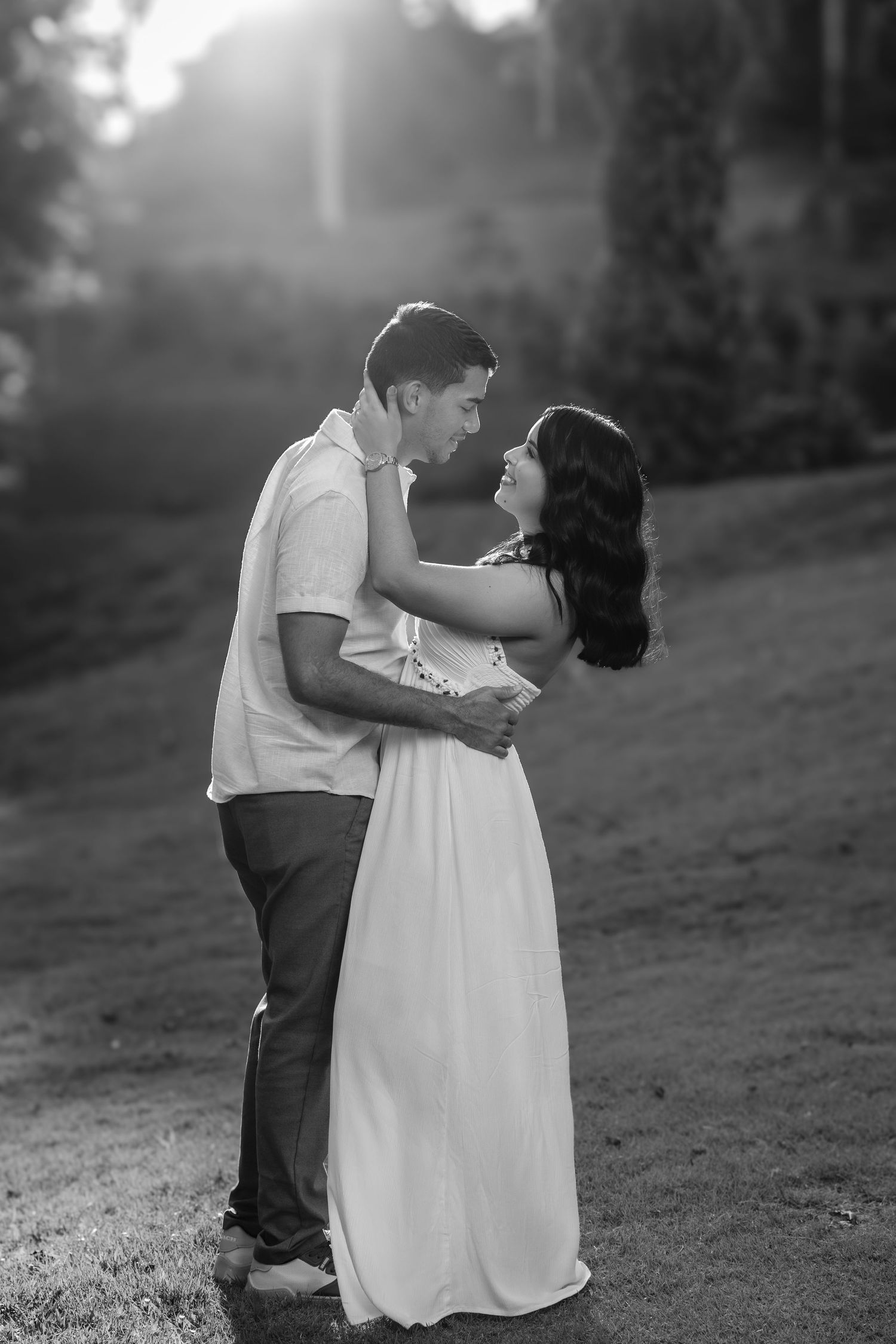 A romantic black and white portrait of a couple embracing on a hillside in the golden hour light.