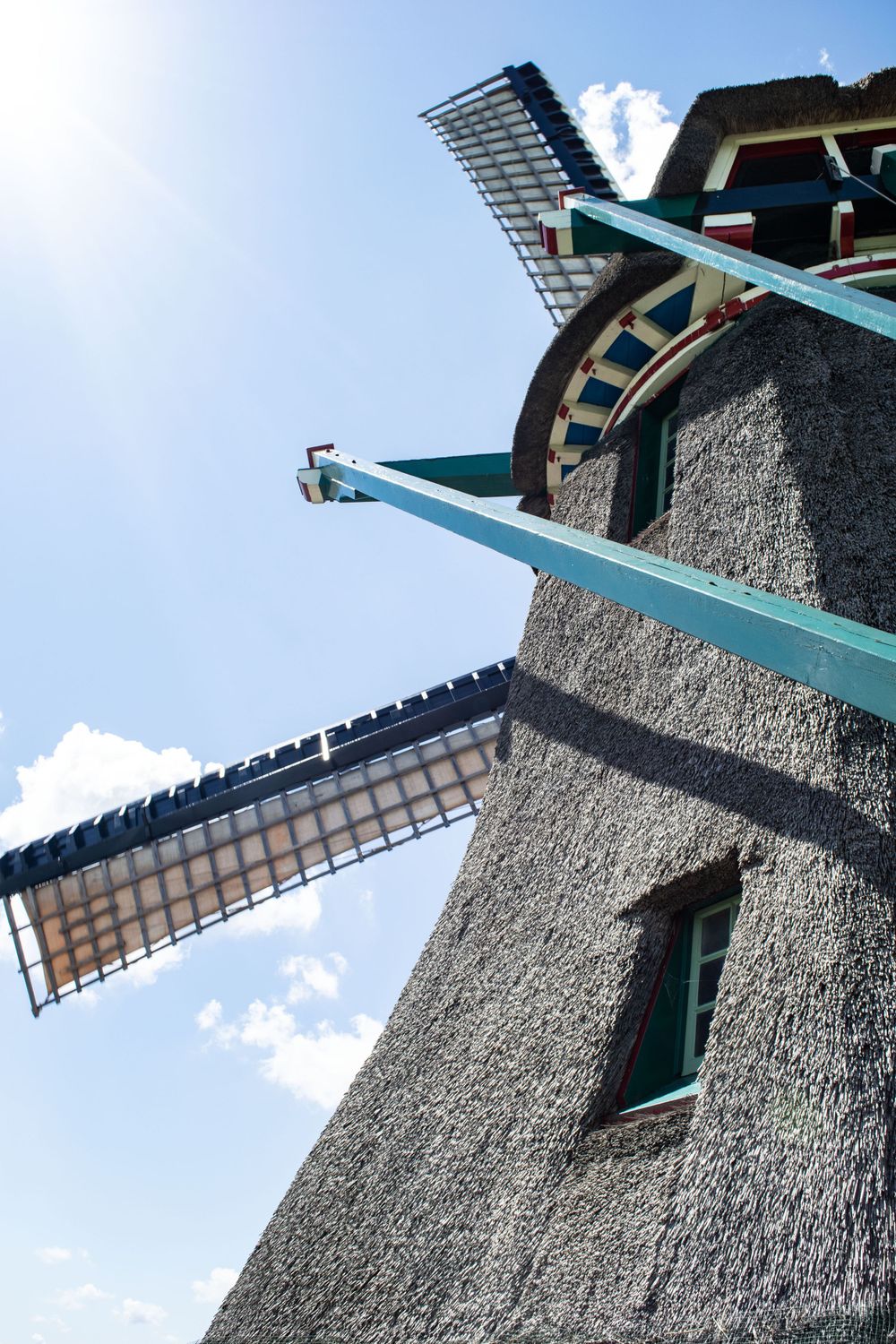 Traditional windmill with white blades against blue sky featuring teal structural supports.