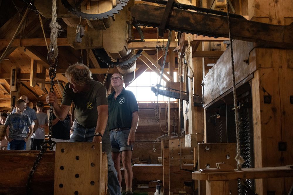 People working inside a rustic wooden mill with machinery and beams.