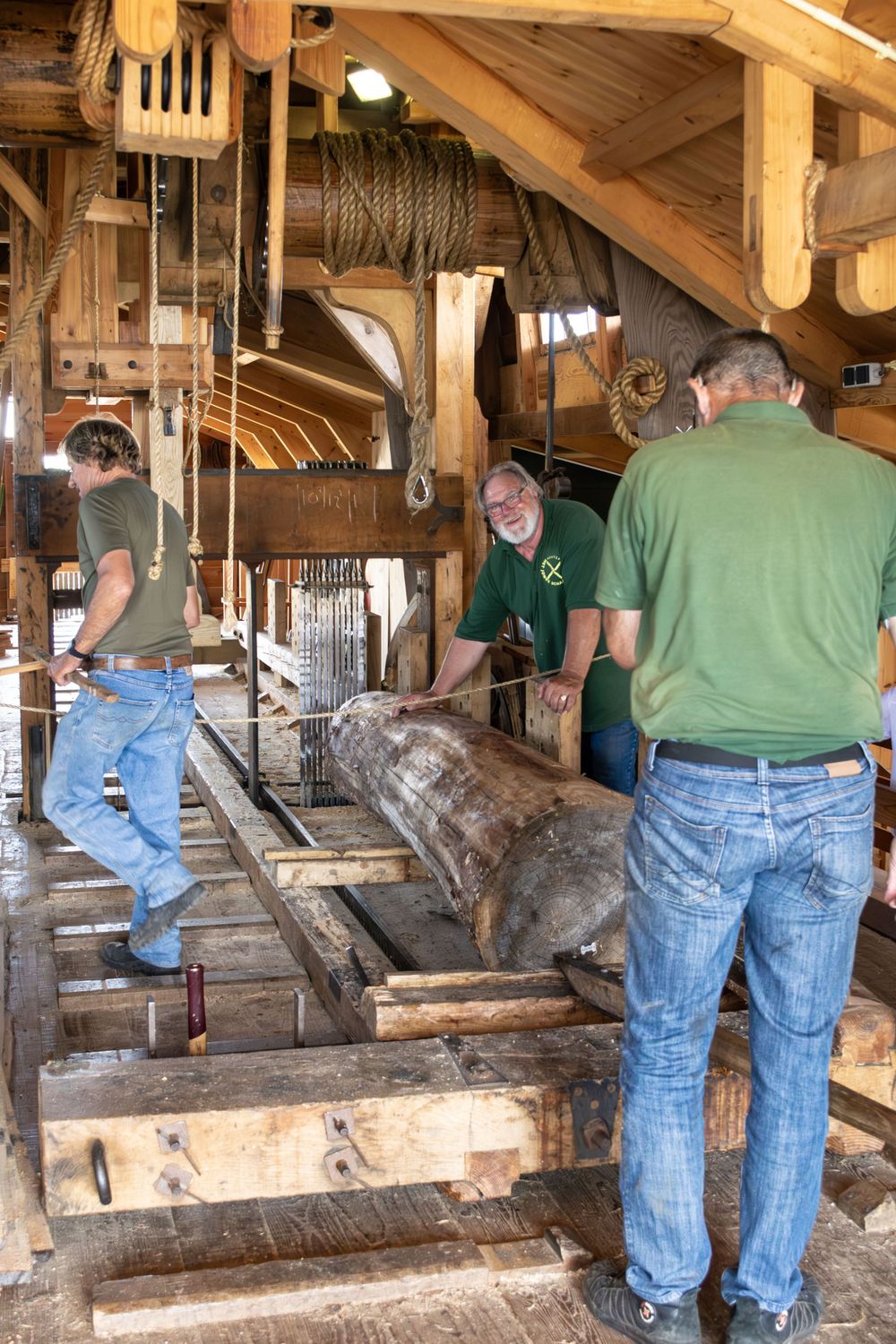 Workers operating historic milling equipment inside a traditional wooden structure.