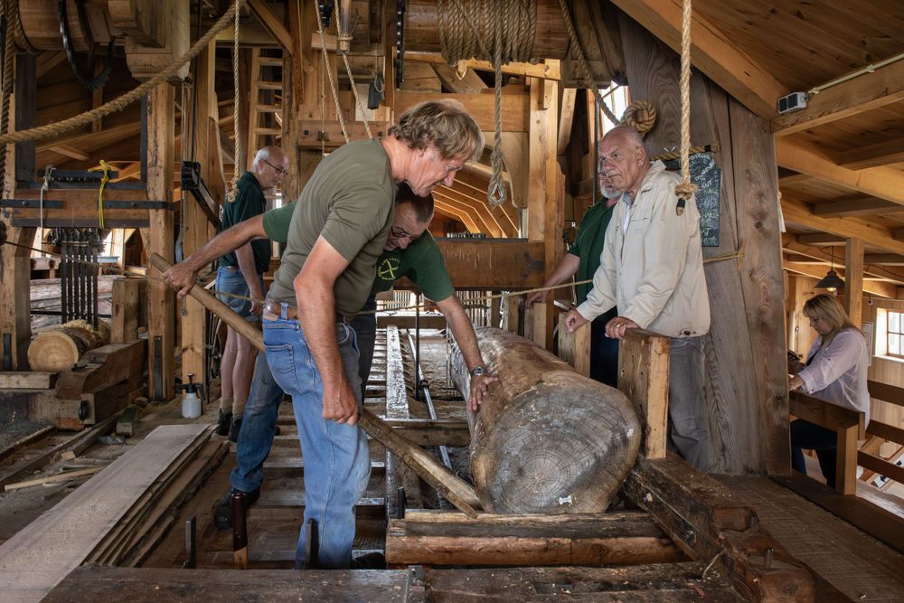 Mill workers inspecting and operating traditional wooden milling equipment.