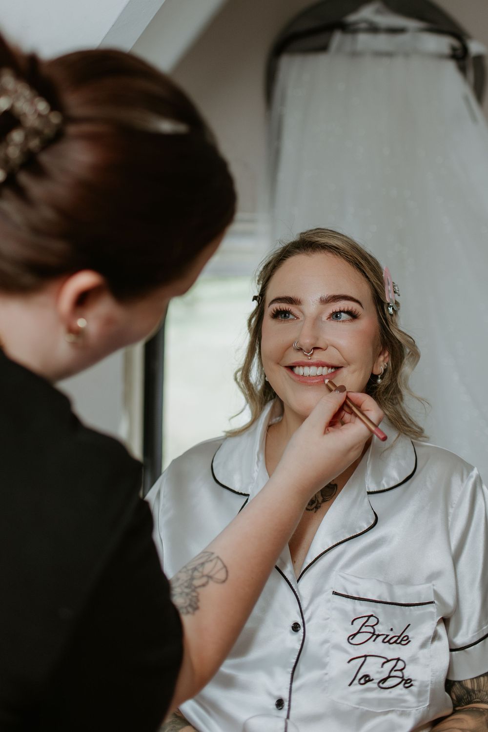 Getting ready for a wedding day wearing white silk pajamas with 'Bride' embroidery during makeup preparations.