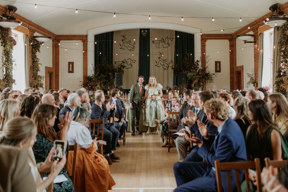 Large wedding reception hall with guests seated at round tables under ornate chandeliers.
