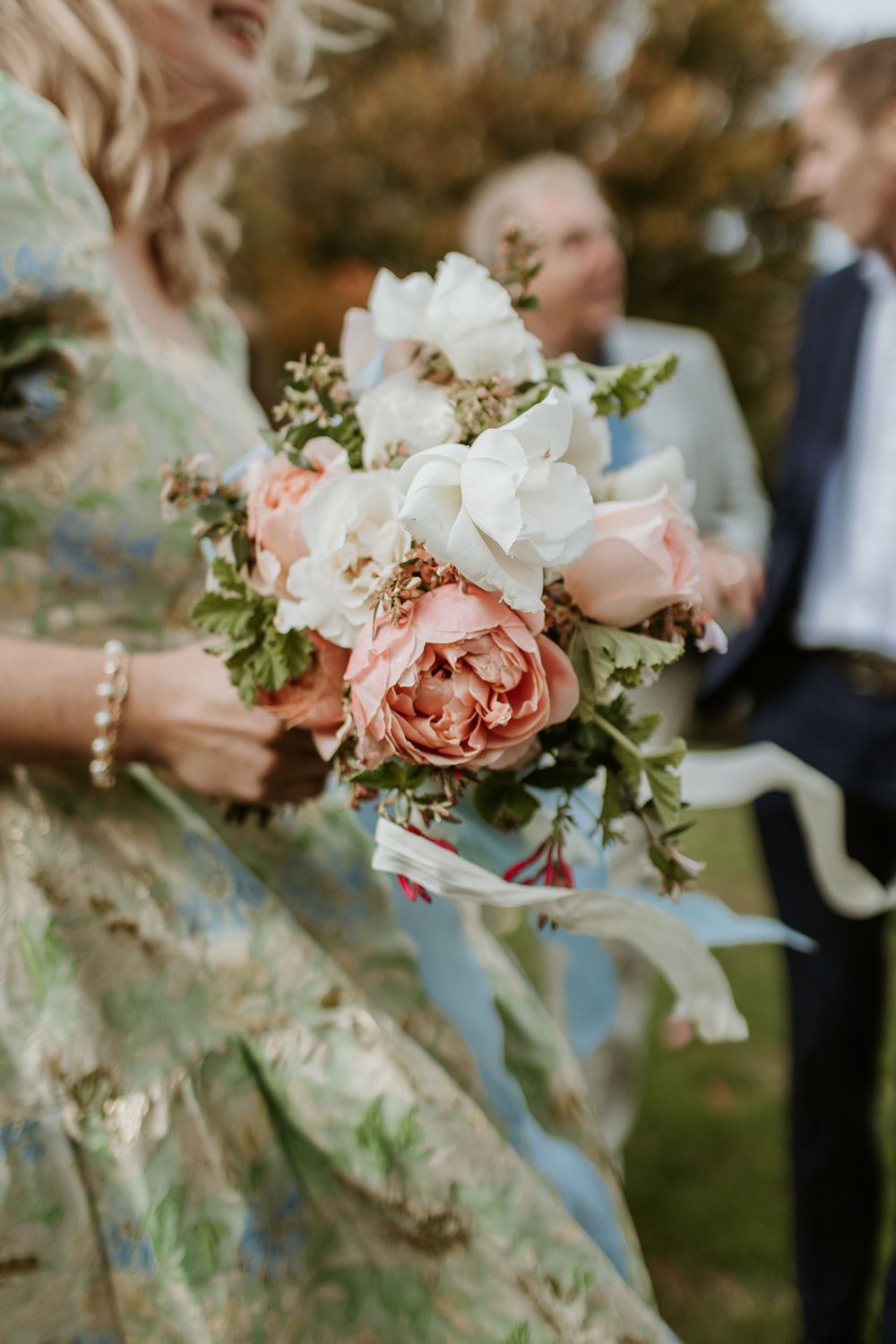 Close-up of romantic wedding bouquet featuring blush pink roses and white flowers with blue ribbon accents.