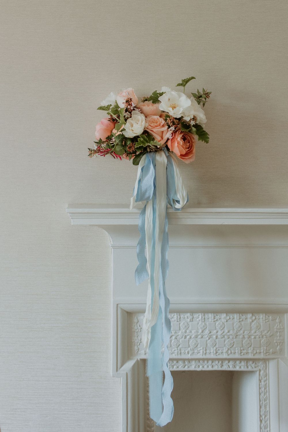 Elegant floral arrangement with pink roses and light blue ribbons cascading down from white mantelpiece.