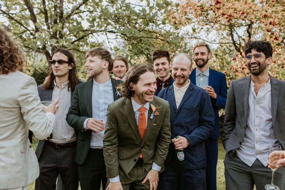 Wedding party laughs together during outdoor autumn photo session in garden setting.