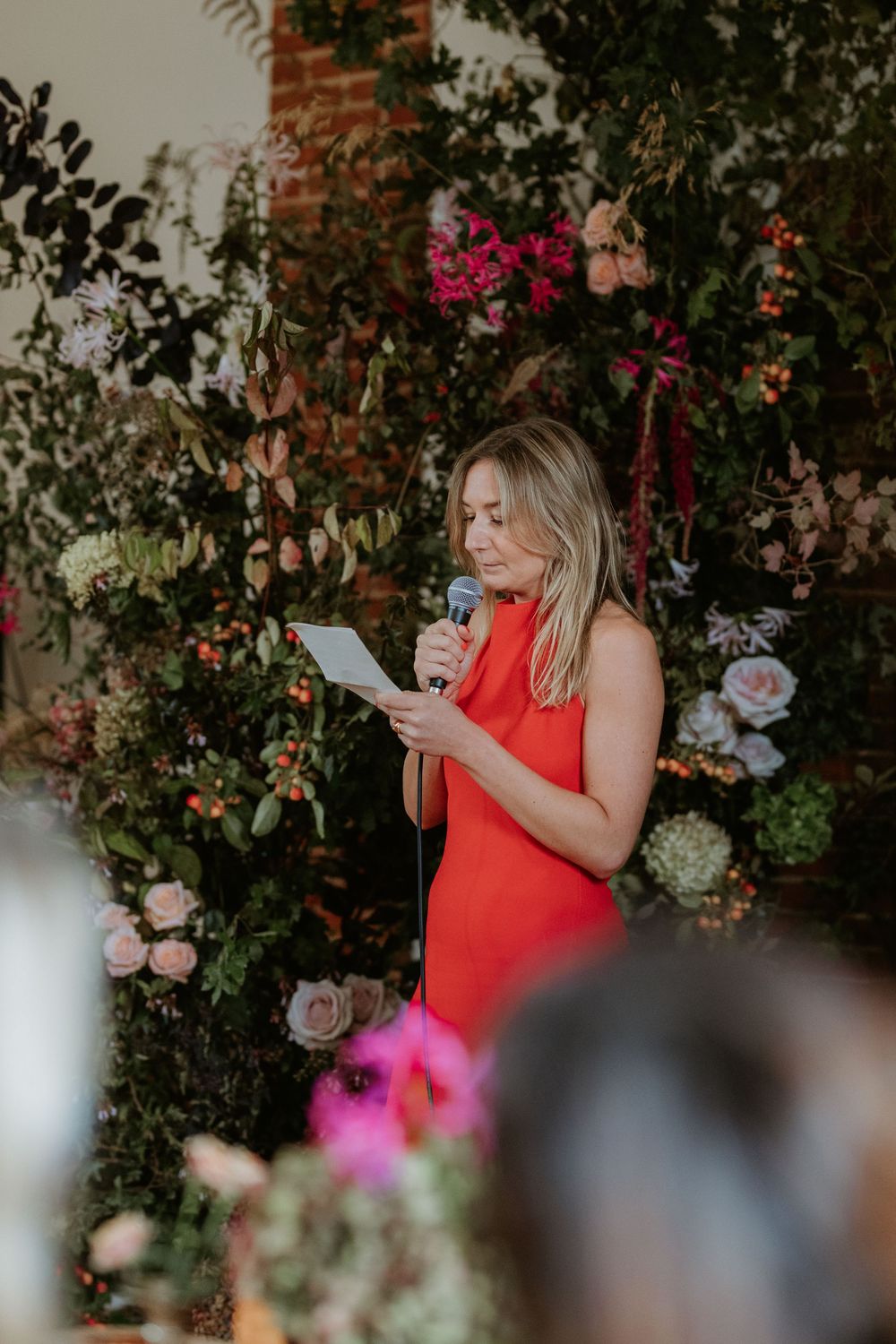 Wedding reception scene with floral decorations and greenery against a brick wall backdrop.