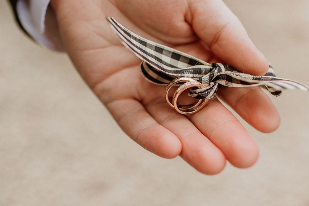 A hand holds wedding rings and a decorative feather against a neutral background.