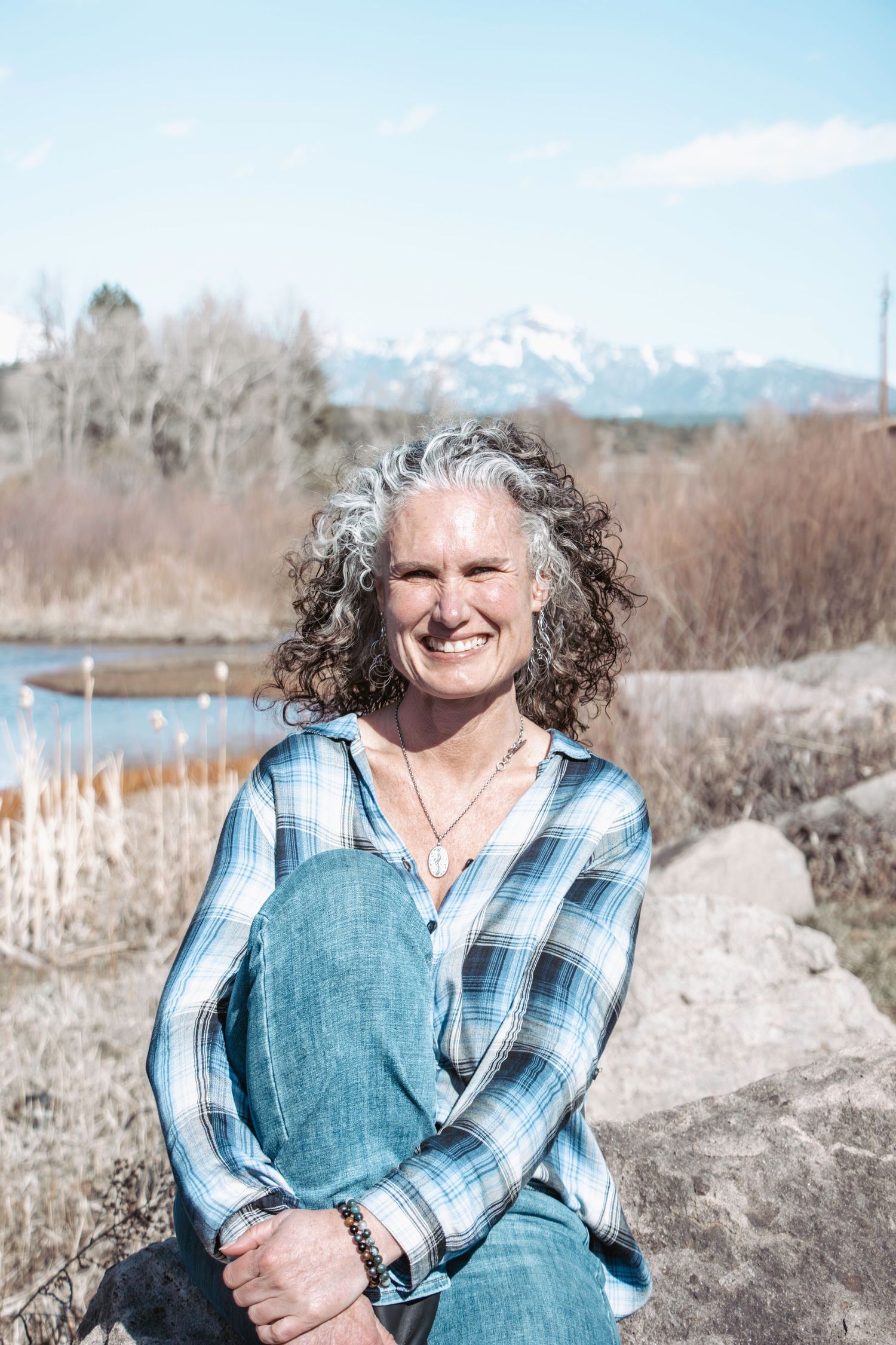 A plaid-shirted figure sits outdoors against a mountainous backdrop with snow-capped peaks and natural scenery.