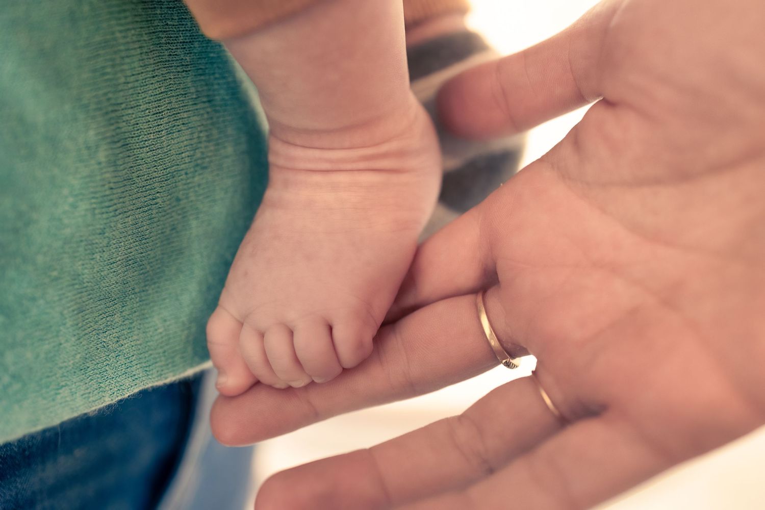 A tiny baby's foot rests gently in an adult's hand against a turquoise background.
