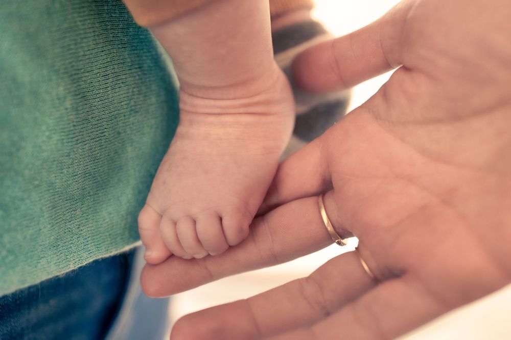 A tiny baby's foot rests gently in an adult's hand against a turquoise background.