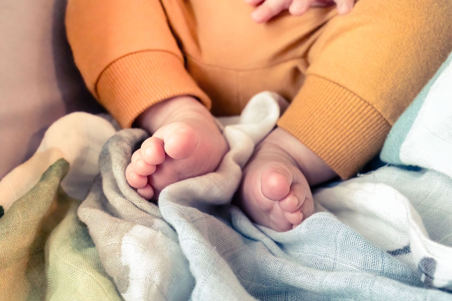Close-up view of tiny baby feet wrapped in a soft gray blanket with orange fabric visible above.