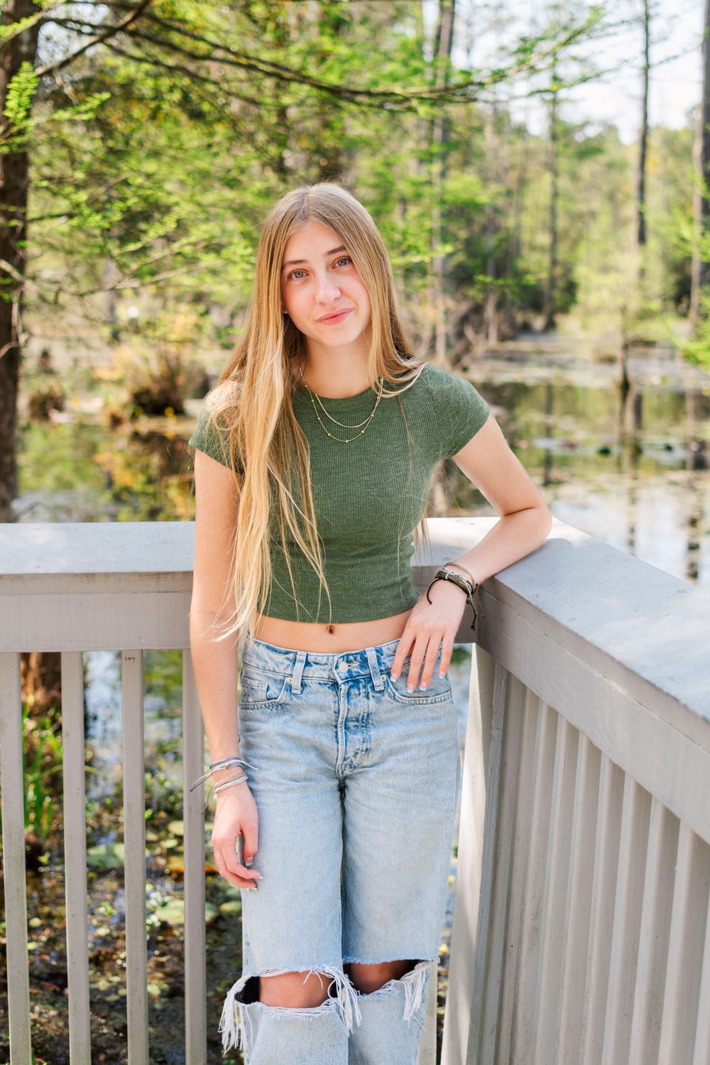 Casual green crop top and distressed jeans outfit photographed on a boardwalk over water.