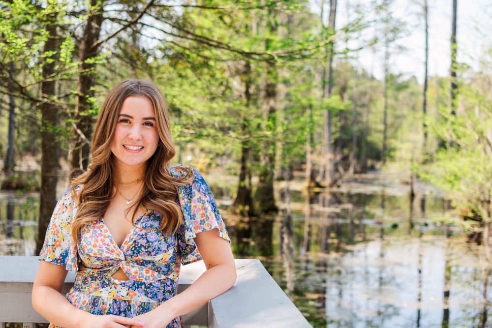 Spring portrait in floral dress on white deck railing with cypress swamp background.