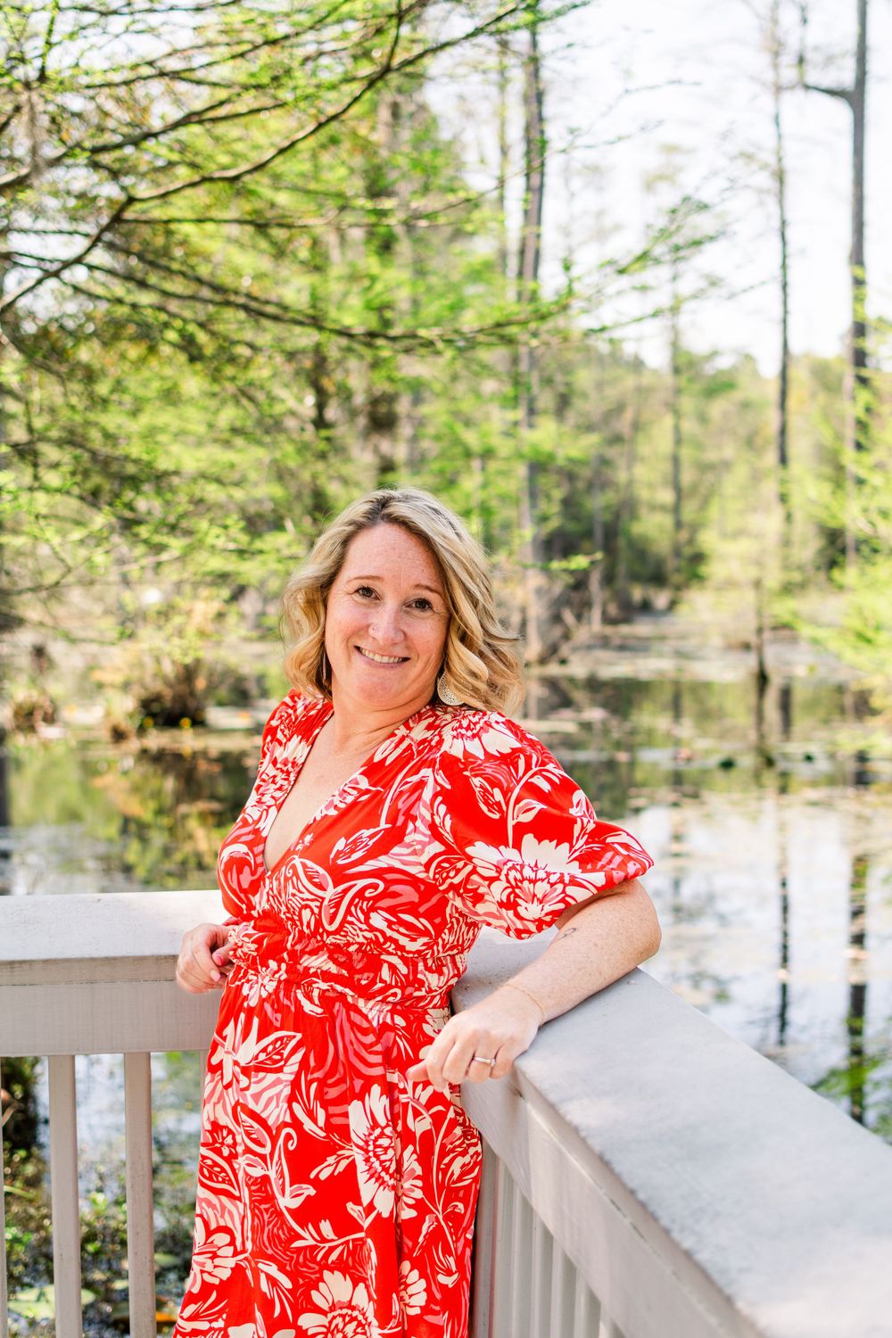 Cheerful outdoor portrait in red and white patterned dress on deck with water view.