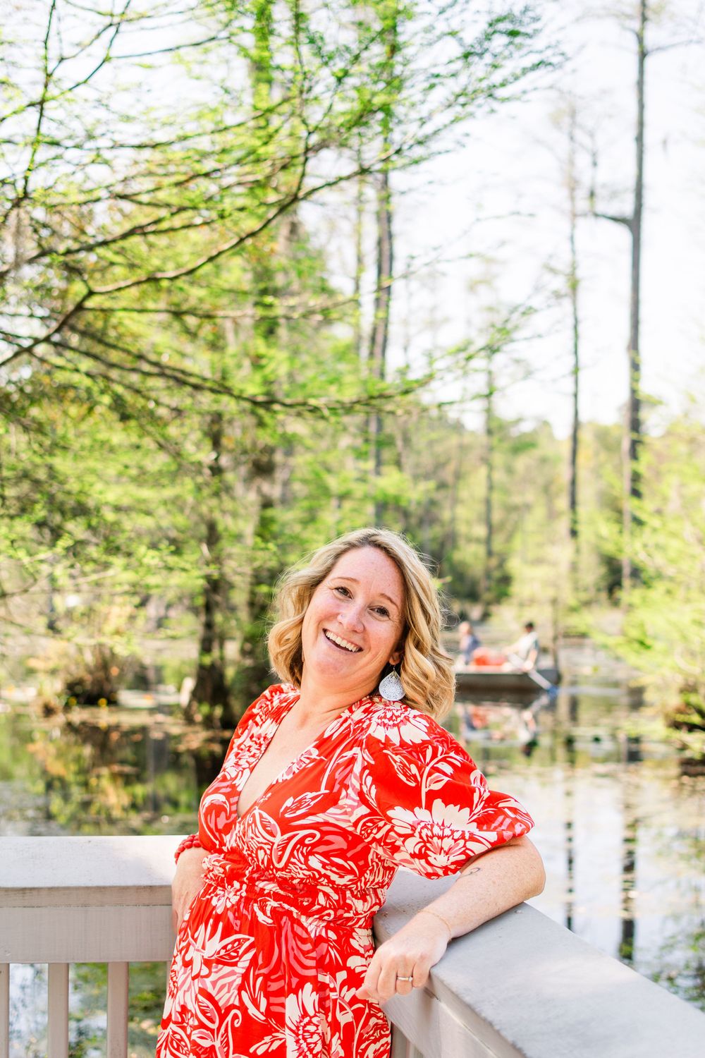 Spring portrait in red floral dress on wooden deck overlooking tranquil pond.