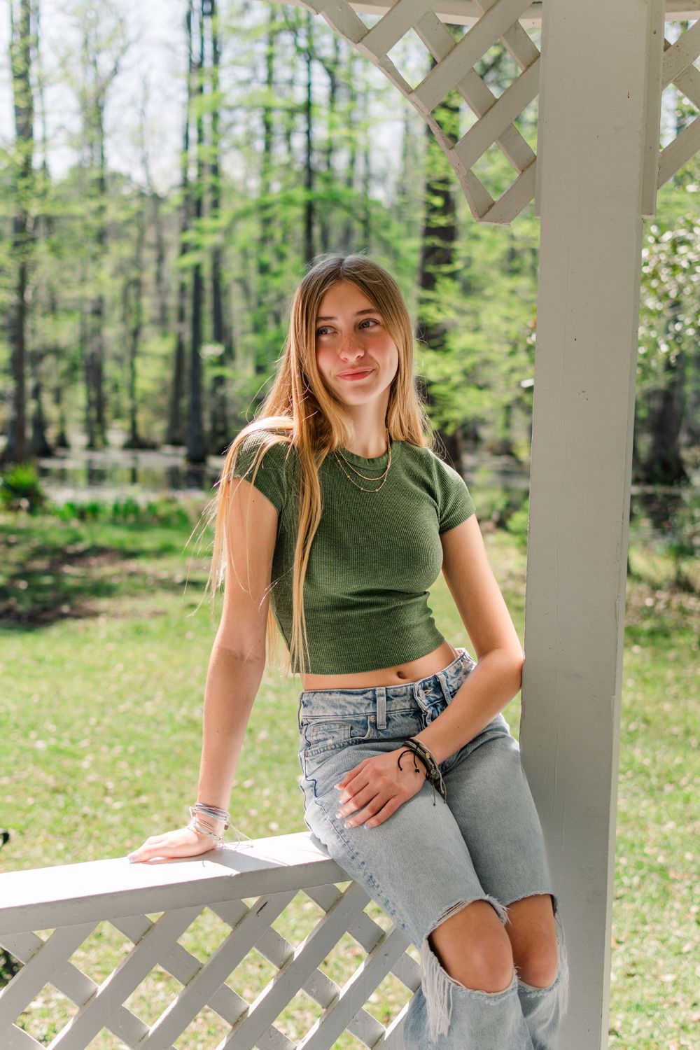 A casual spring outdoor portrait featuring a green crop top and distressed jeans on a white lattice porch.