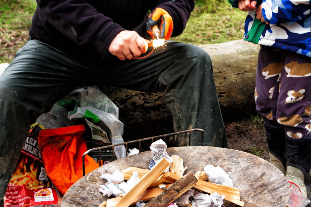 Person in work gloves preparing firewood and kindling on a rustic outdoor surface.