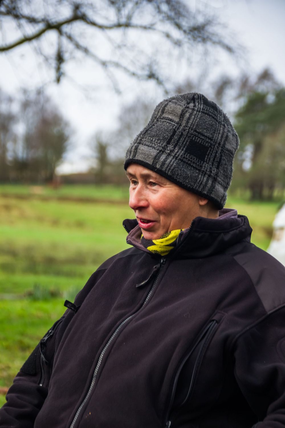 Person wearing winter hat and dark jacket outdoors in rural setting.