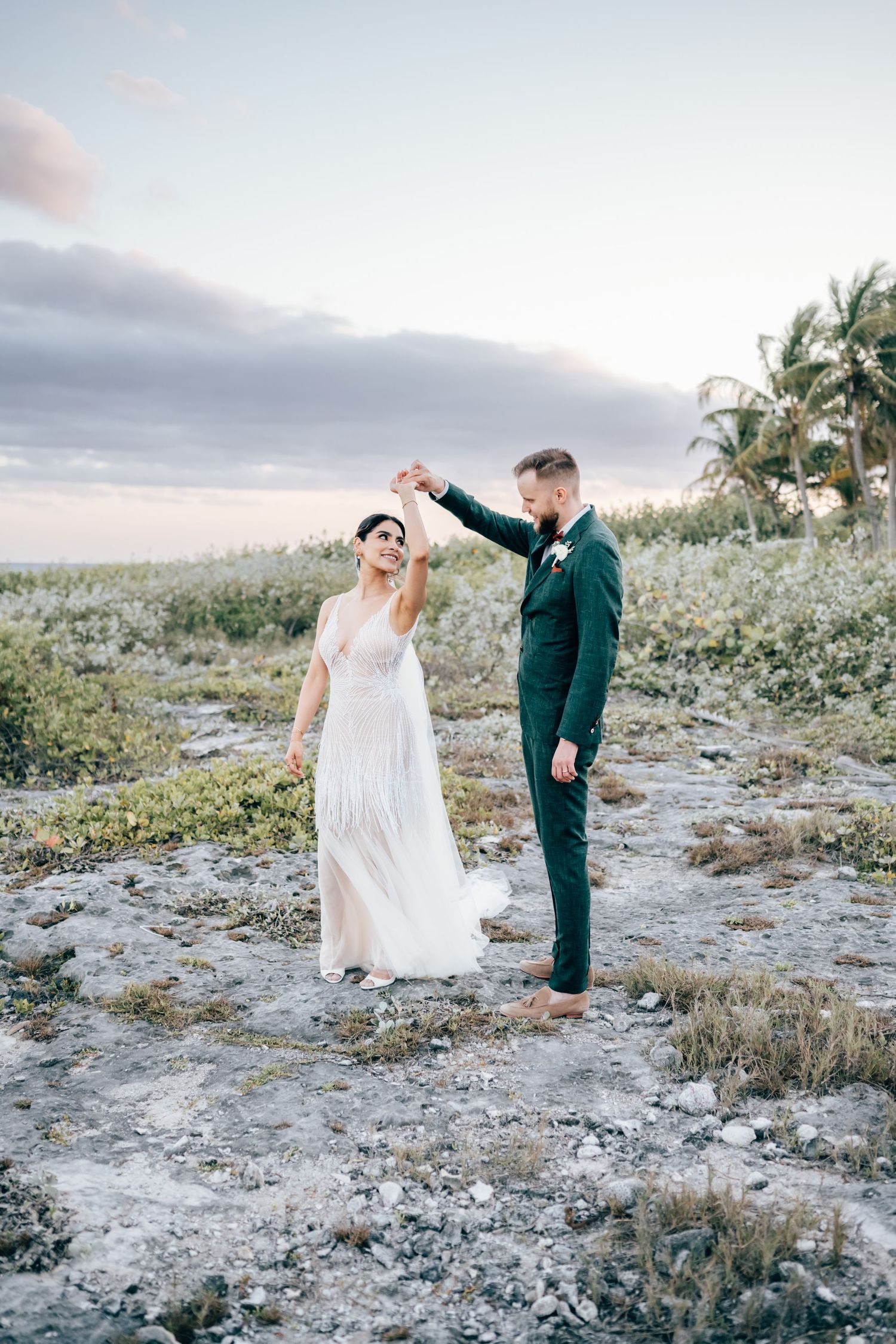 A romantic moment captured on a rocky coastal landscape at sunset with palm trees in the background, Blue Venado, Mango Weddings.
