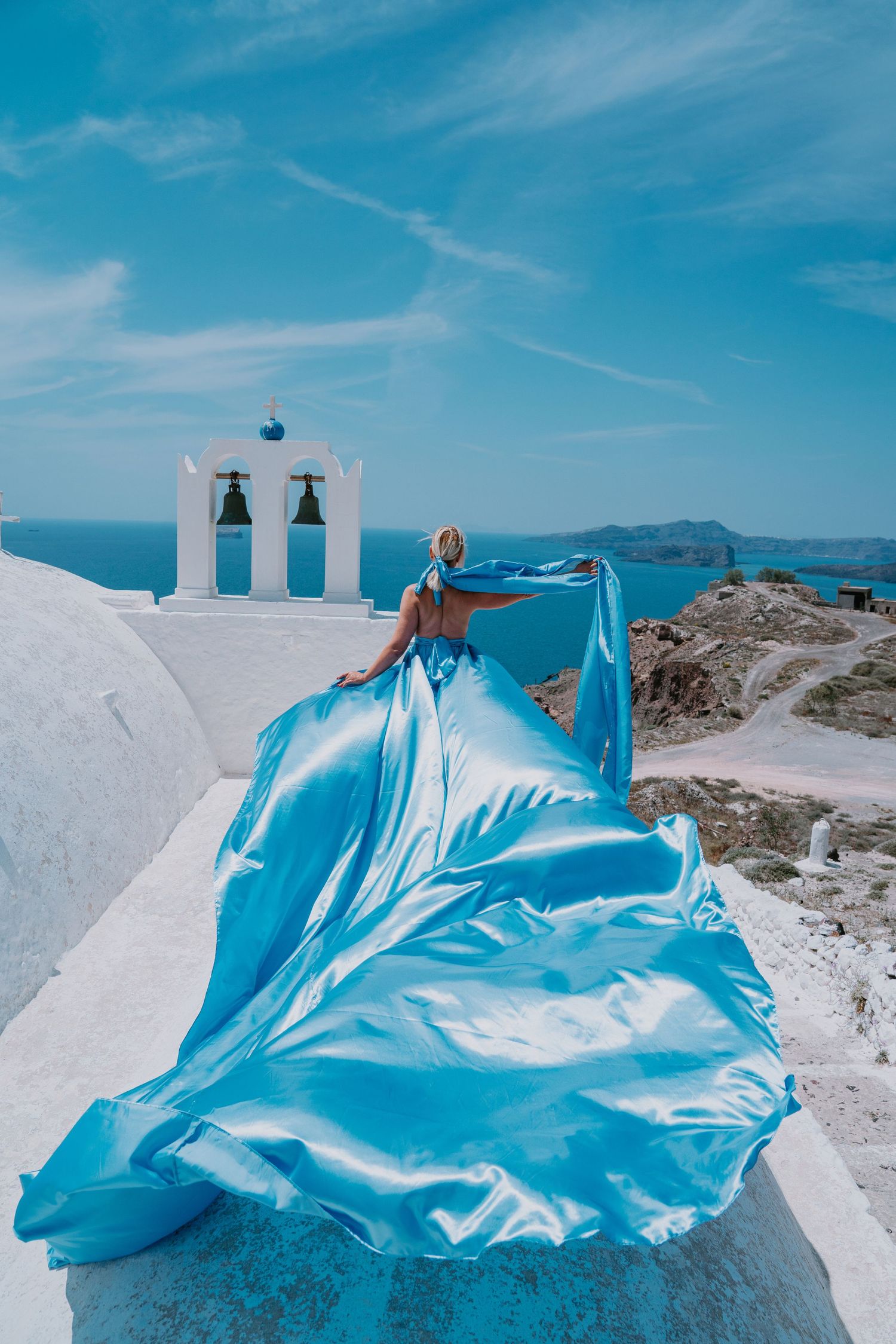 Flowing turquoise dress photographed near white bell tower overlooking Mediterranean Sea.