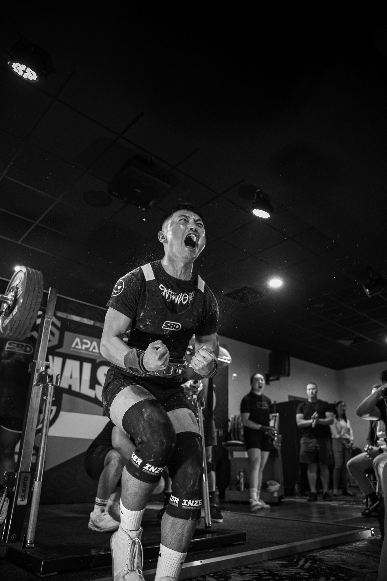 Intense weightlifting moment captured in black and white at indoor gym competition.
