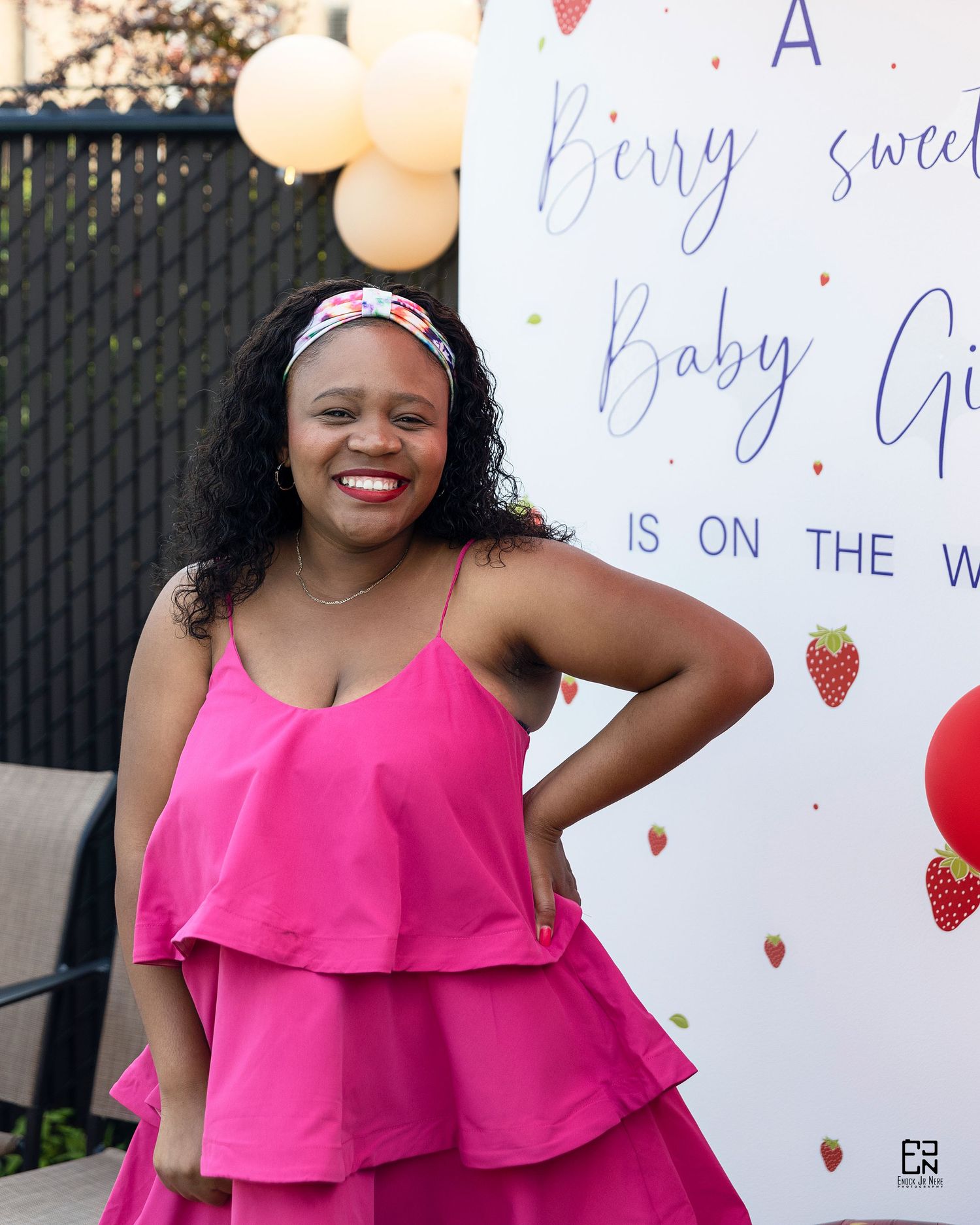 Celebratory photo with pink ruffle dress against baby shower backdrop with balloons.