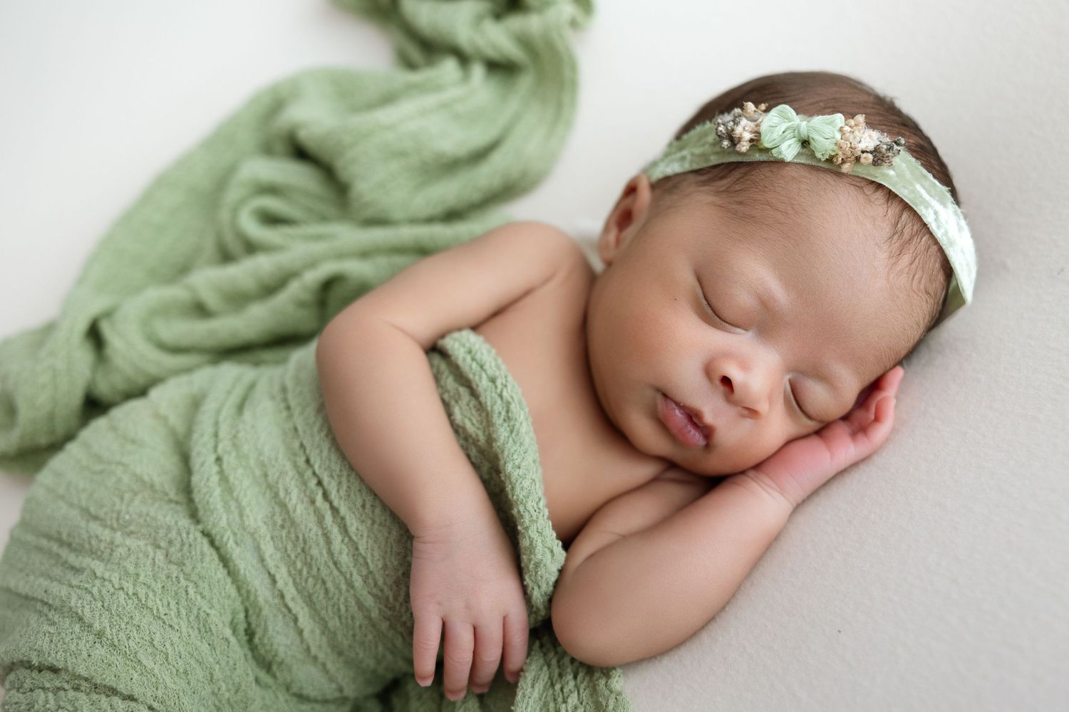 A child in a white dress holds a sleeping newborn wrapped in tan fabric on a furry cream background.